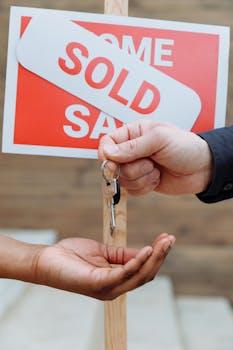 pexels photo 8482876 8482876 Hands exchanging house keys in front of a sold sign, symbolizing real estate success.